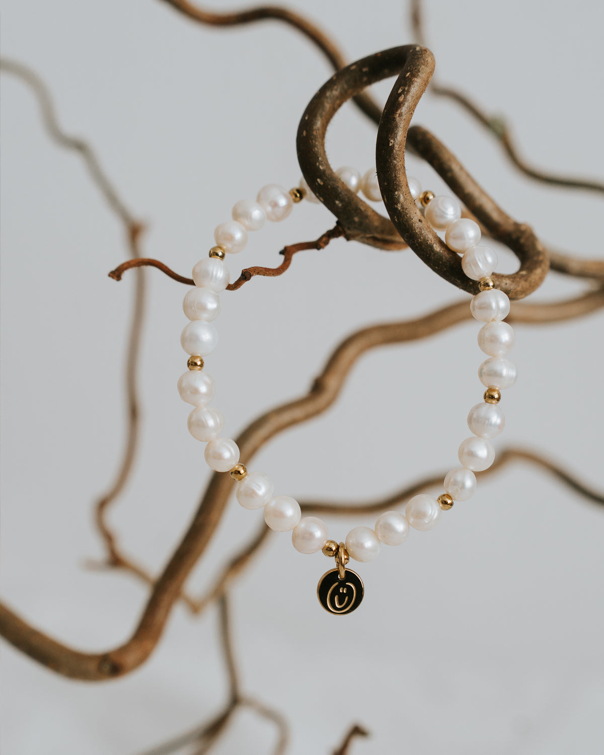 Süßwasserperlen-Armband in Gold zwischen Zweigen.