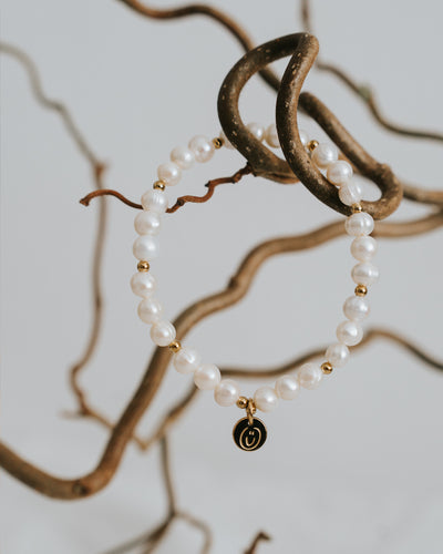 Süßwasserperlen-Armband in Gold zwischen Zweigen.