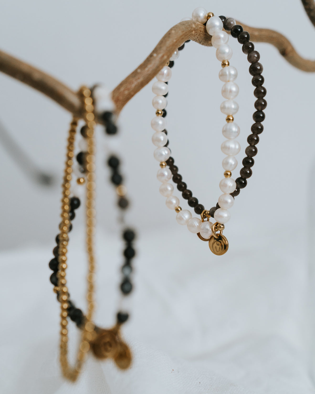 Süßwasserperlen-Armband in Gold neben Obsidian-Armband arrangiert.