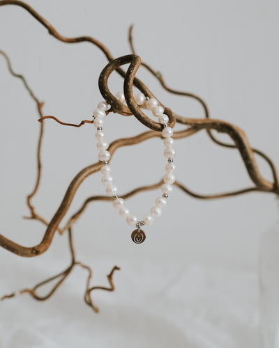 Süßwasserperlen-Armband in Silber zwischen Zweigen.