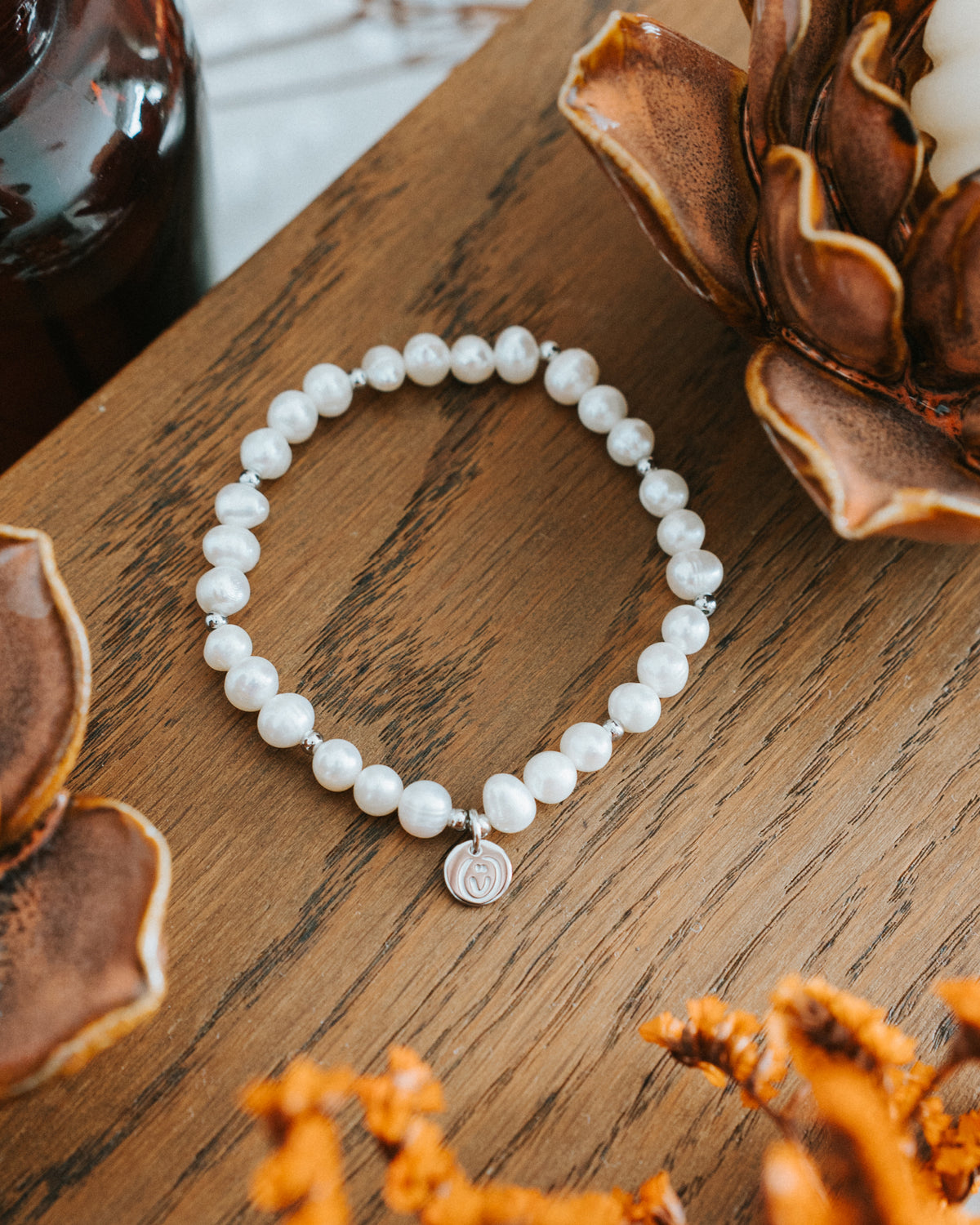 Süßwasserperlen-Armband in Silber auf Holz mit Trockenrose.