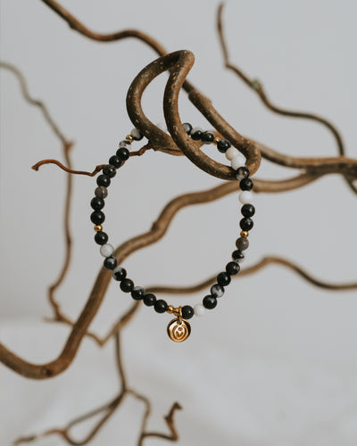Zebra-Jaspis-Armband in Gold zwischen Zweigen.