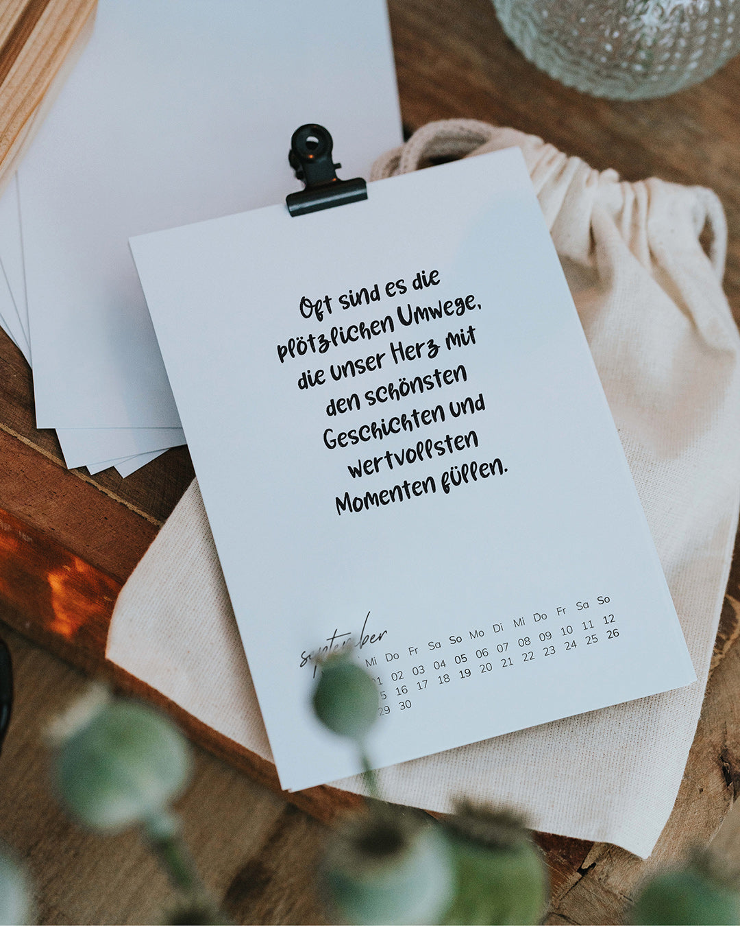 September-Karte des Tischkalenders 2027 mit Foldback-Klammer, liegend auf Holz neben Baumwollbeutel
