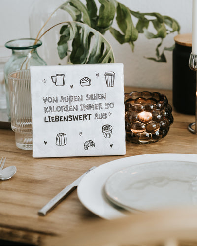 Serviette mit Kalorien-Spruch aufgestellt zwischen Teller und Windlicht – bringt gute Laune an den Tisch.