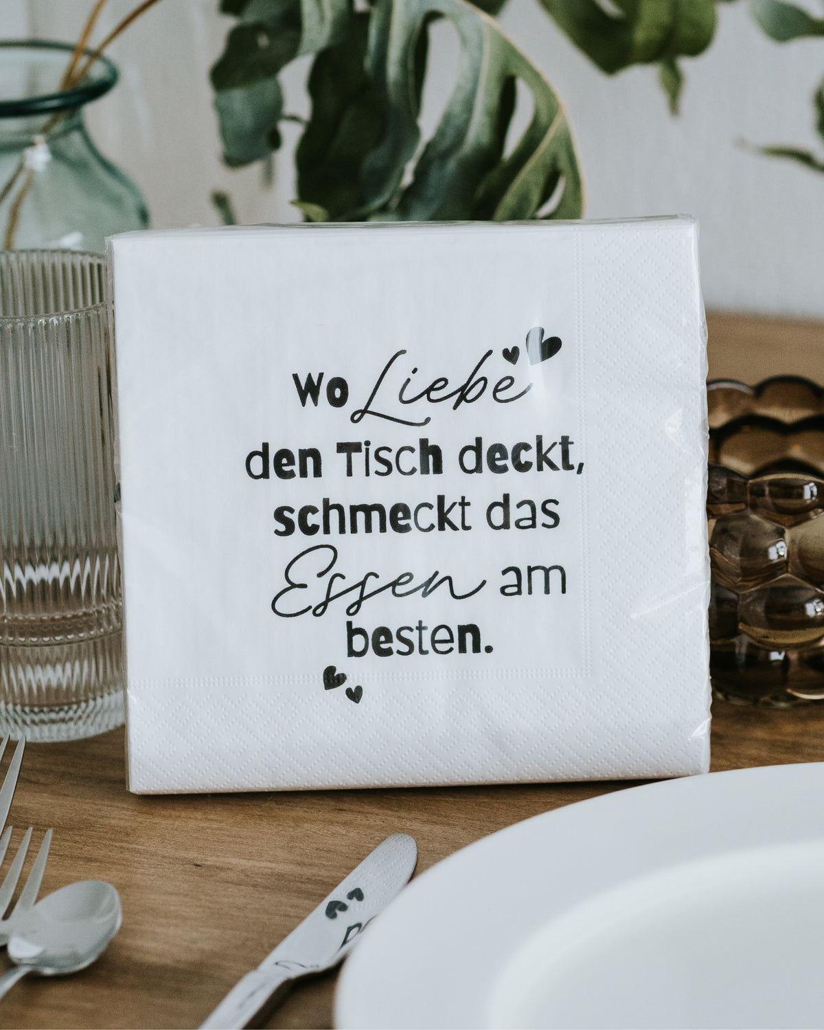 Serviette mit Spruch „Wo Liebe den Tisch deckt, schmeckt das Essen am besten.“ auf gedecktem Tisch.