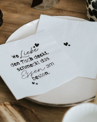 Zwei Servietten mit Spruch „Wo Liebe den Tisch deckt“ auf dem Teller – stabil, saugfähig und stilvoll.