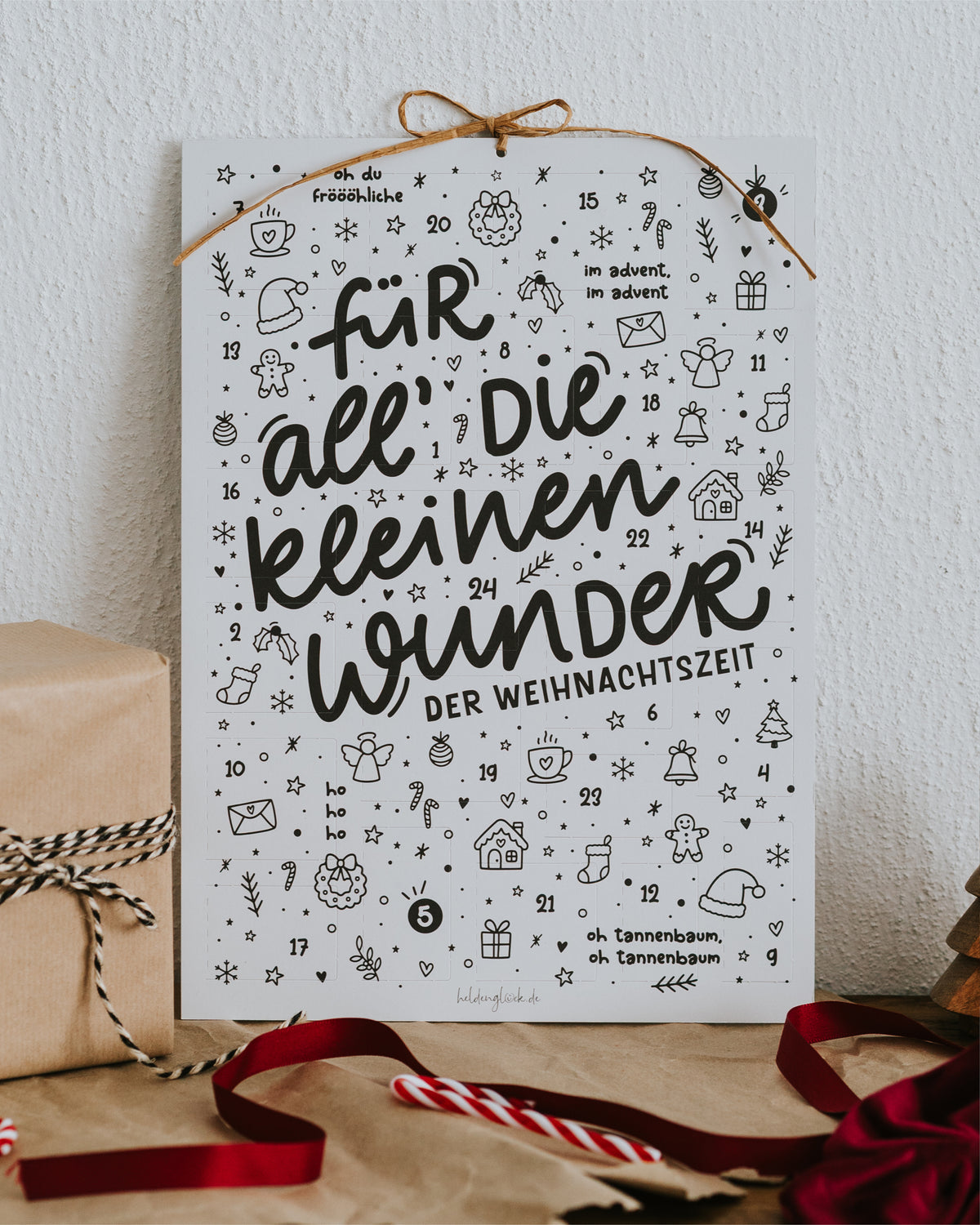 Adventskalender „Für all die kleinen Wunder der Weihnachtszeit“ mit Aufhängekordel, daneben Geschenke und Zuckerstange.