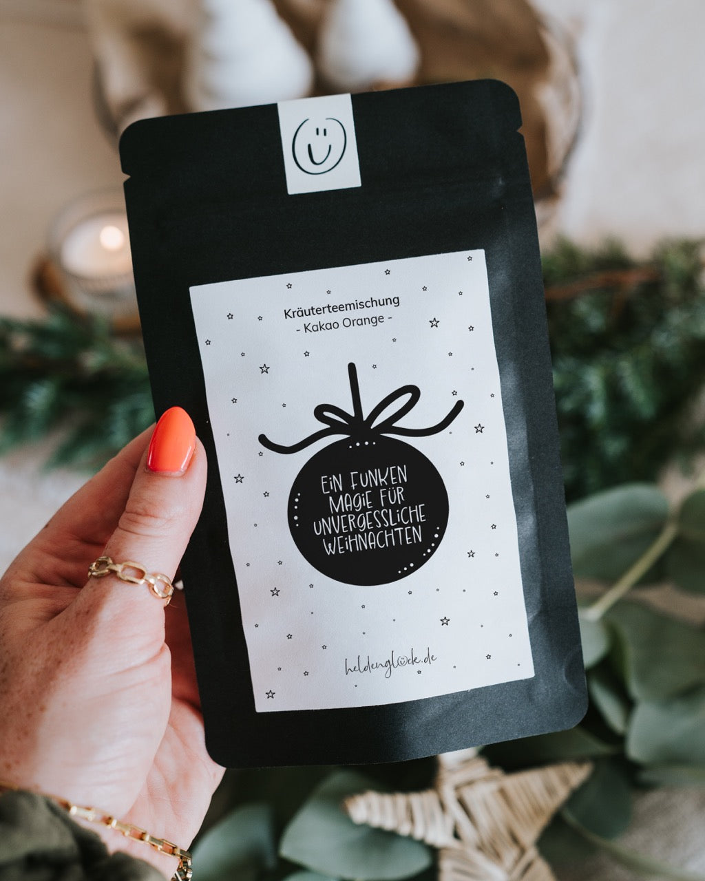 Hand hält Weihnachtstee „Ein Funken Magie für unvergessliche Weihnachten“, Kräuterteemischung Kakao-Orange.