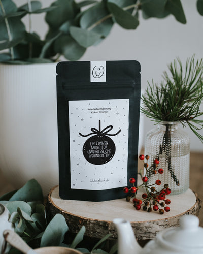 Weihnachtstee „Ein Funken Magie“ auf Holzscheibe mit Eukalyptus, Kiefernzweig und Hagebutten.