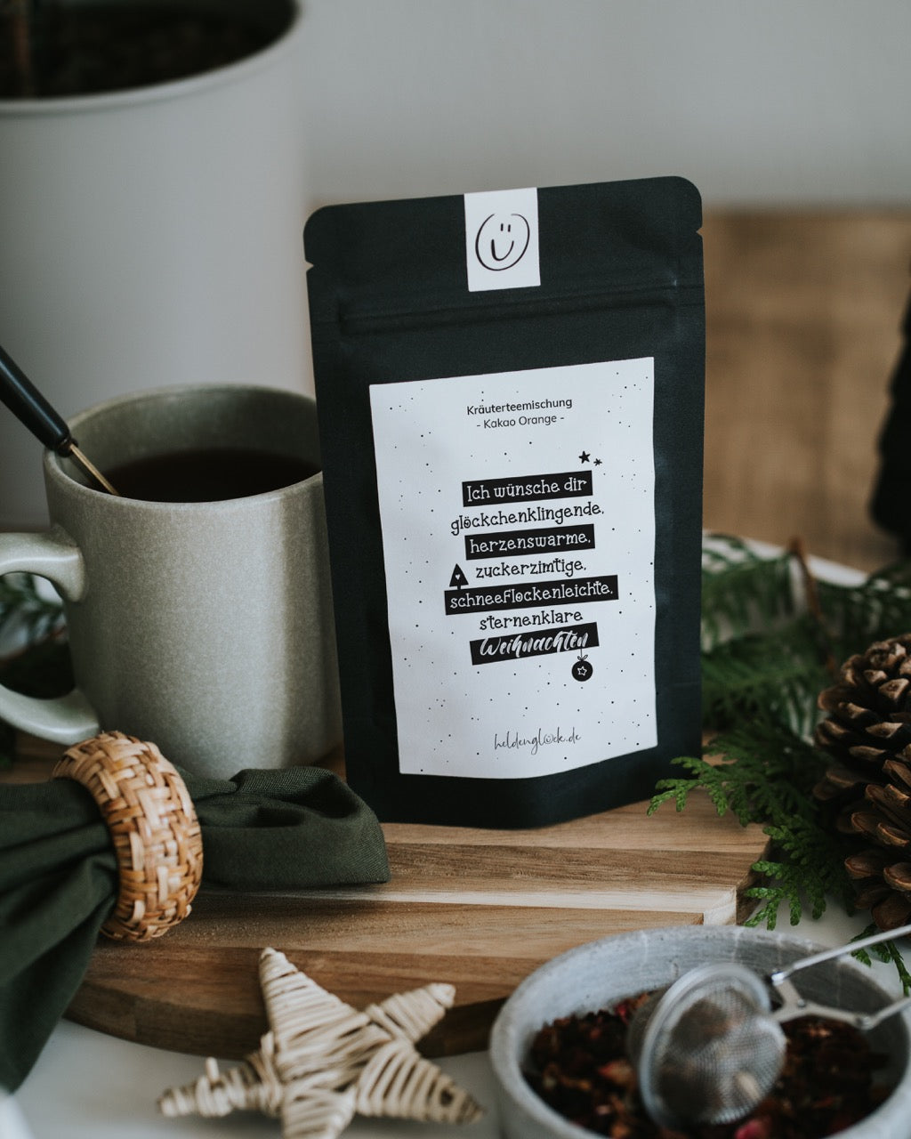Weihnachtstee „Glöckchenklingende Weihnachten“ neben Tasse und Schale mit losem Tee – Tasse und Deko nicht enthalten.