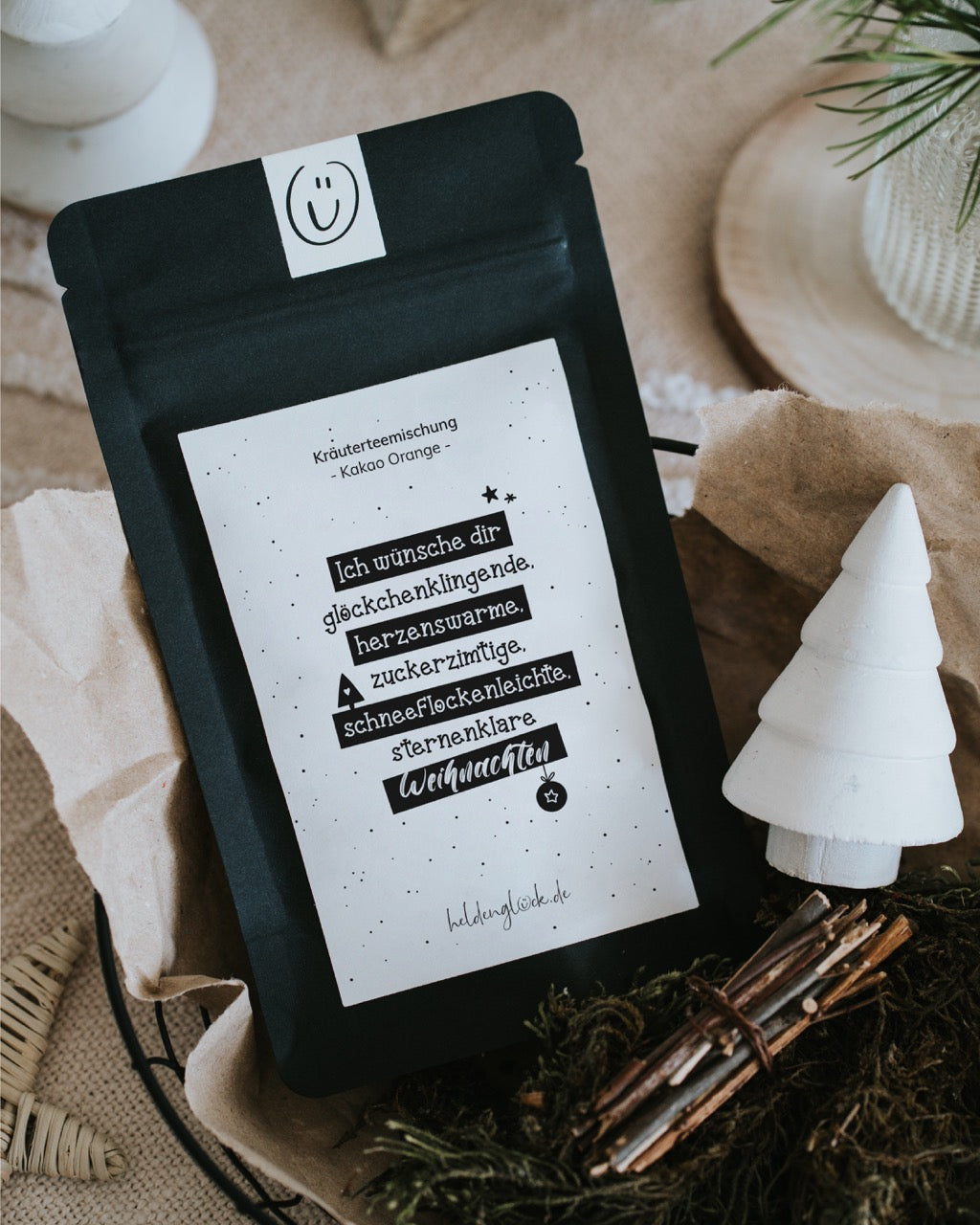 Weihnachtstee „Glöckchenklingende Weihnachten“ auf Papier mit Deko-Tanne und Zimtstangen.