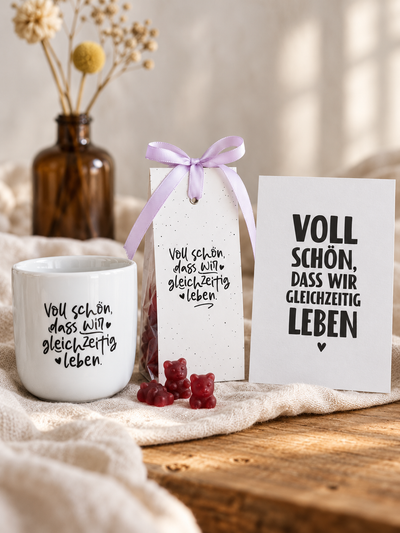 Voll-schön-Geschenkset mit Porzellanbecher, Cranberry-Vanille-Teebären und Postkarte auf hellem Leinen.