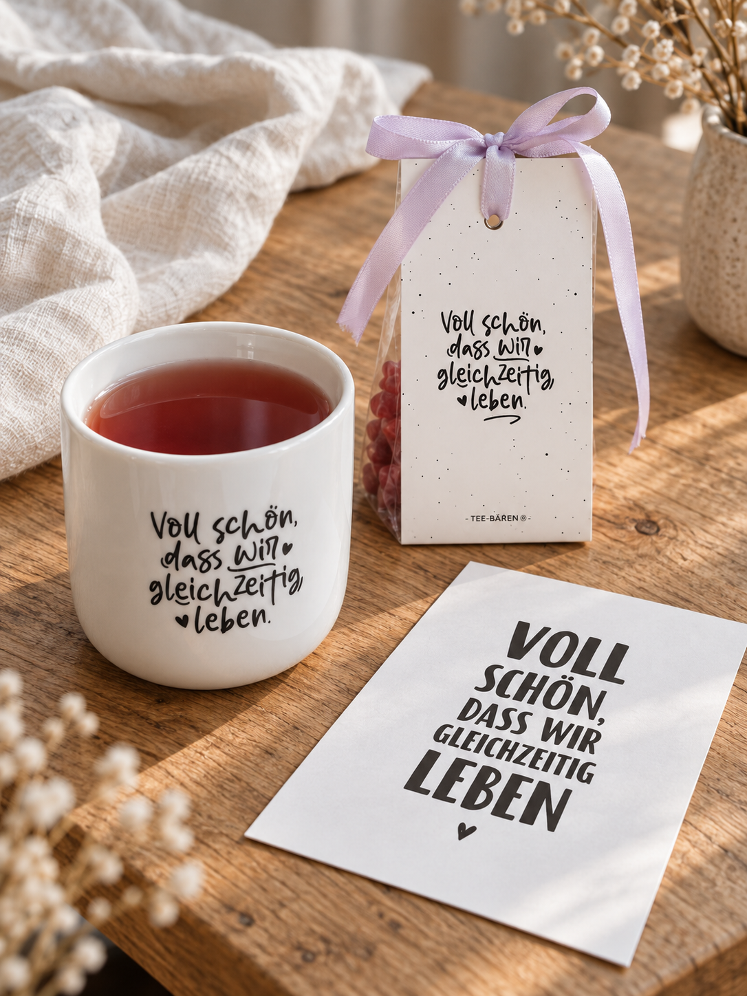 Voll-schön-Geschenkset als Teepause mit Becher, Teebären und Postkarte auf einem Holztisch.