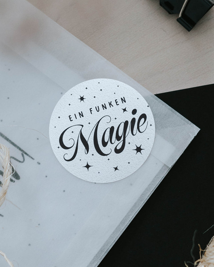 Streifen mit 5 Aufklebern „Ein Funken Magie“ neben Schere, Washi-Tape und gestreifter Geschenktüte