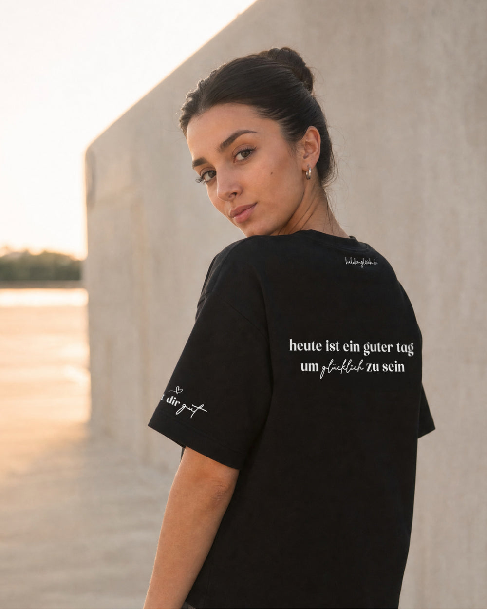 Frau im schwarzen T-Shirt von schräg hinten; auf dem Rücken steht „heute ist ein guter tag um glücklich zu sein“.