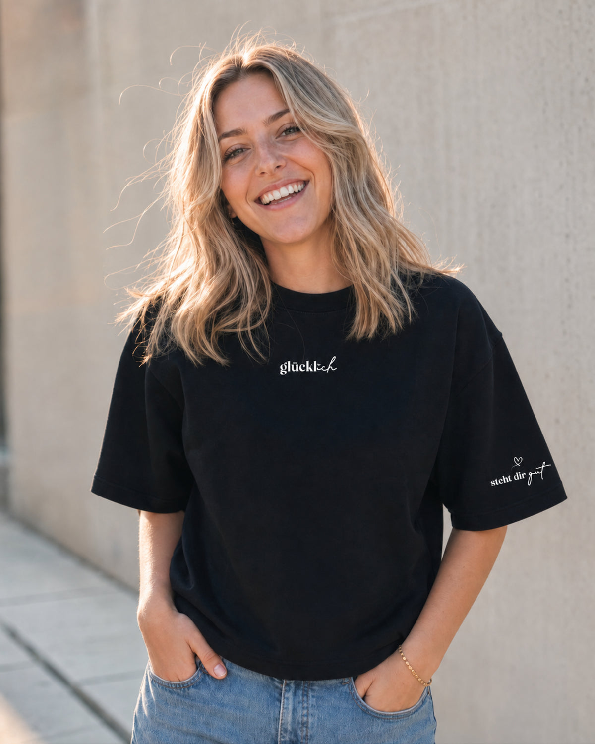 Vorderseite des schwarzen T-Shirts an einer Frau, mit kleinem weißen Schriftzug „glücklich“ auf der Brust.
