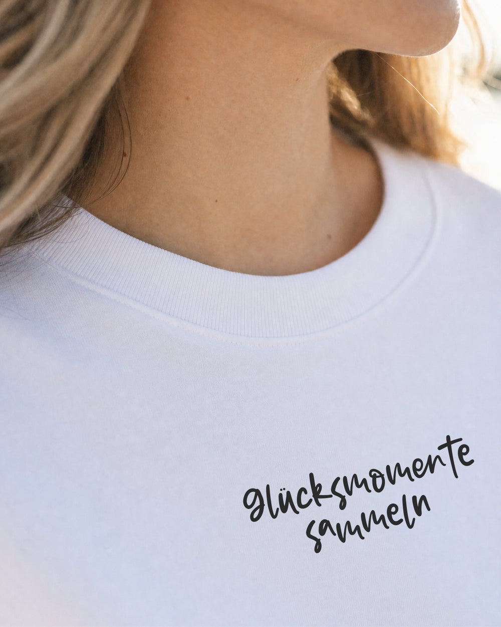 Nahaufnahme des Brustaufdrucks „Glücksmomente sammeln“ auf dem weißen T-Shirt.