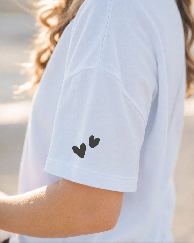 Detail des weißen T-Shirt-Ärmels mit zwei kleinen schwarzen Herzen.