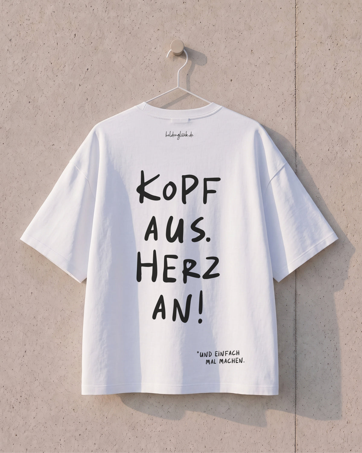 Weißes T-Shirt am Bügel mit großem Rückenprint „Kopf aus. Herz an!“ und dem Zusatz „und einfach mal machen.“