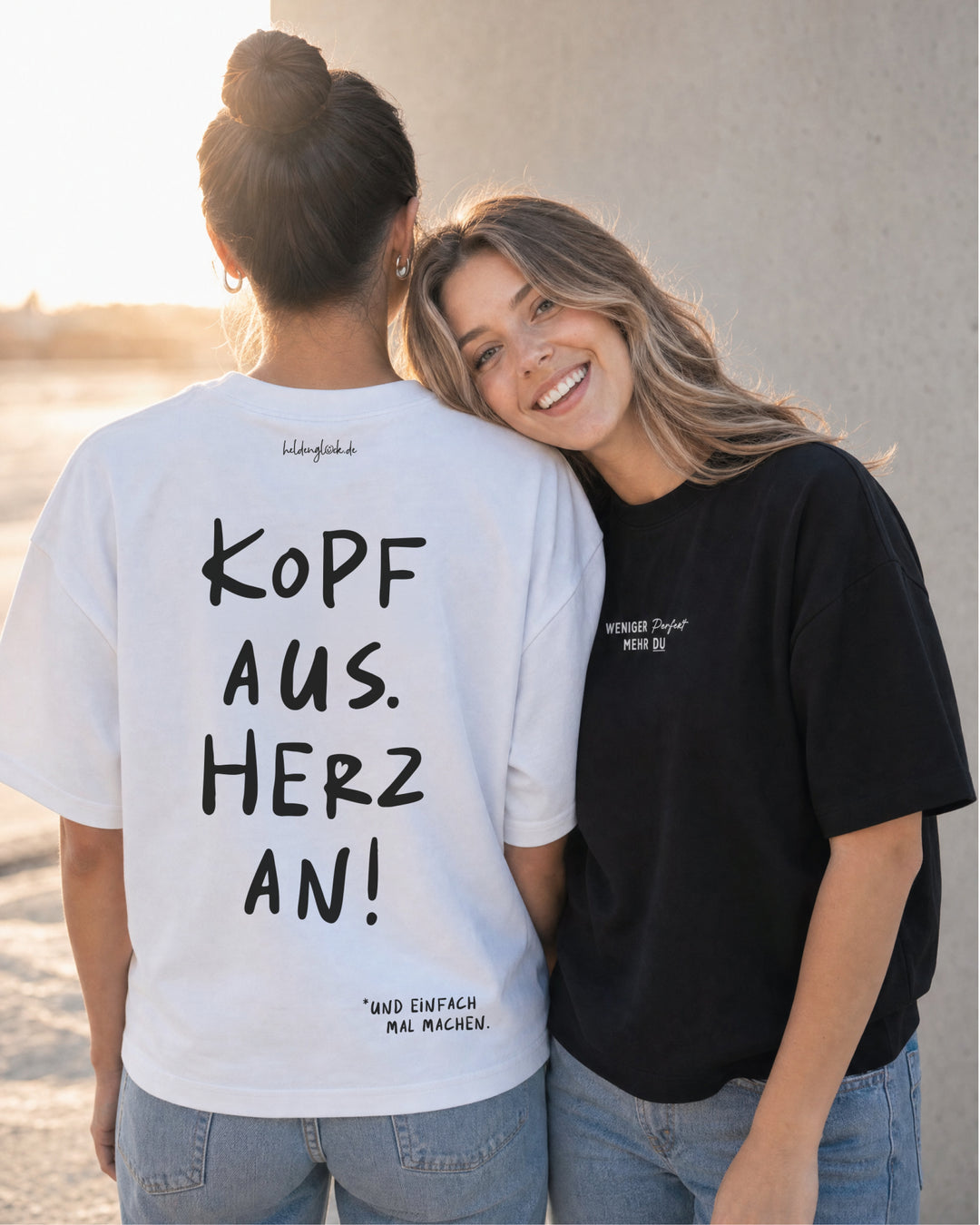 Zwei Frauen nebeneinander; eine zeigt den Rücken des weißen T-Shirts „Kopf aus. Herz an!“, die andere trägt ein schwarzes Shirt.