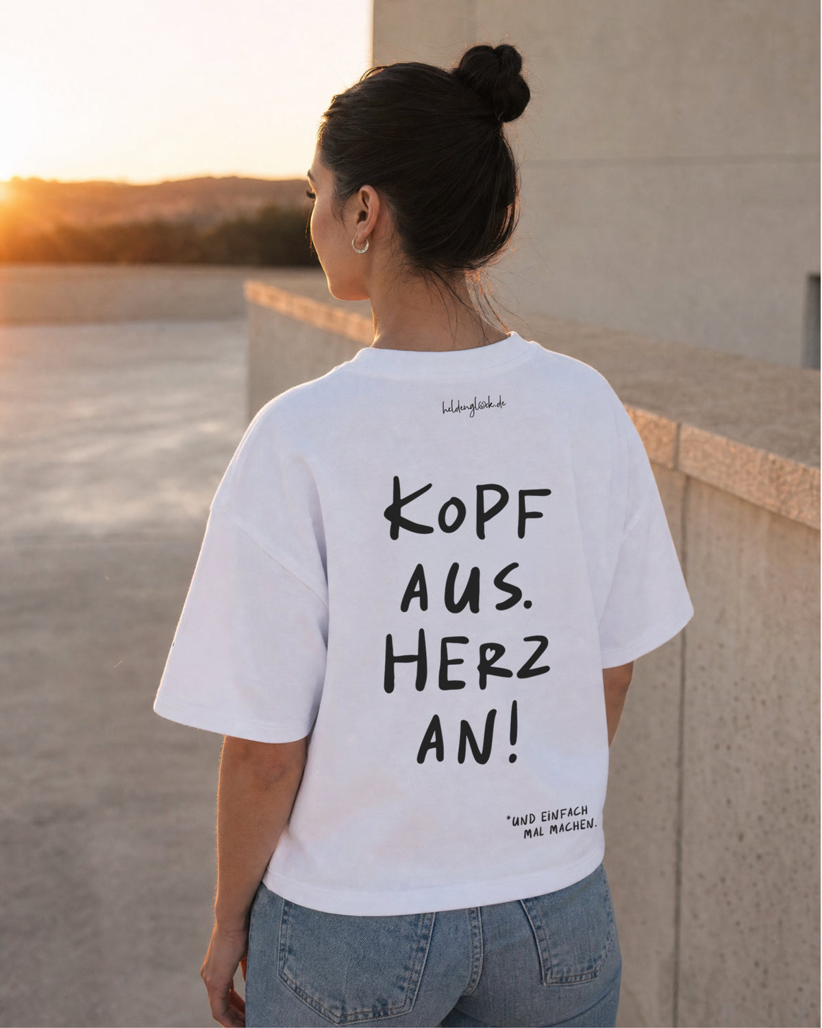 Frau von hinten im weißen T-Shirt mit dem Rückenprint „Kopf aus. Herz an!“ und locker fallenden Ärmeln.