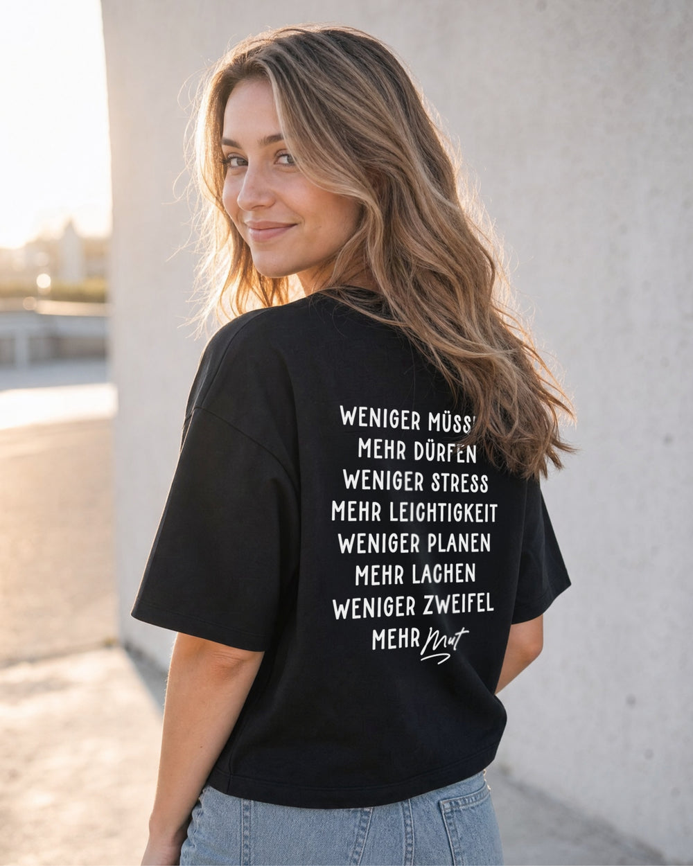 Frau im schwarzen T-Shirt „Weniger perfekt, mehr du“ von schräg hinten, mit weißem Spruchdruck über mehrere Zeilen.