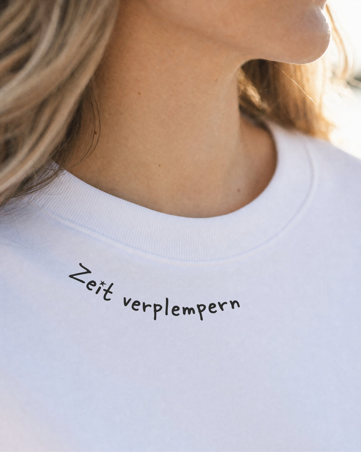 Nahaufnahme des weißen T-Shirts mit dem Brustprint „Zeit verplempern“.