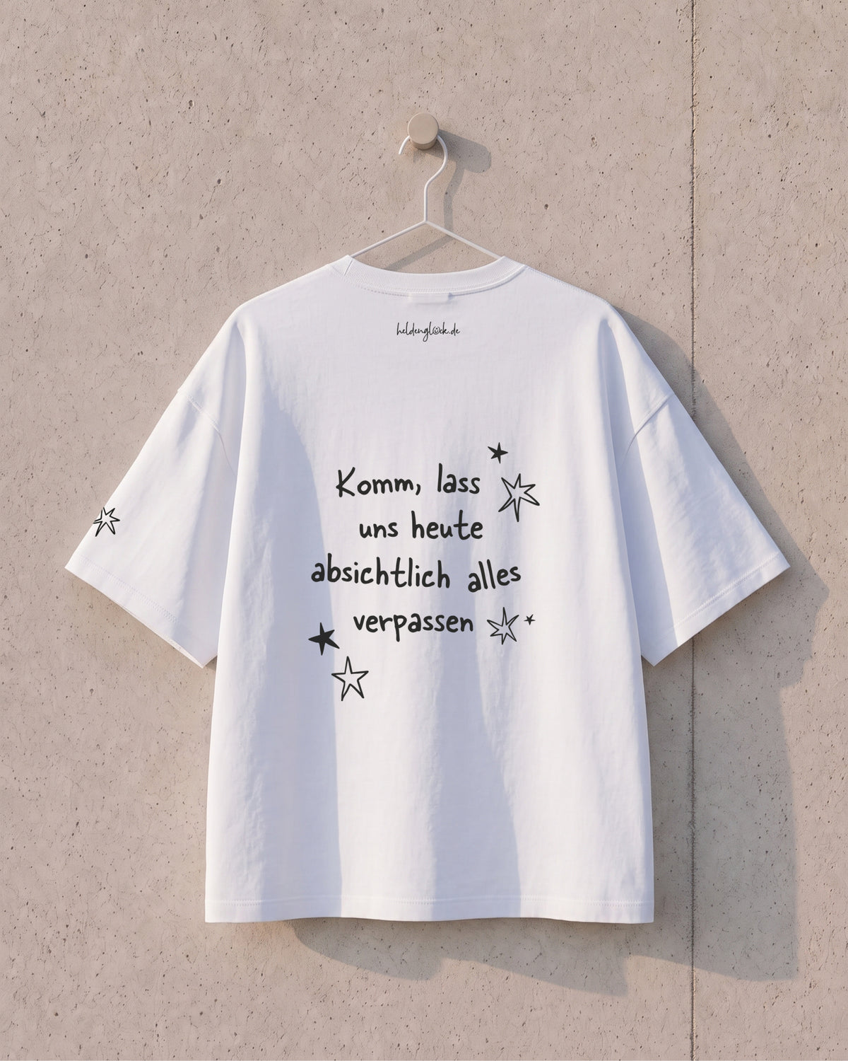 Rückseite des weißen T-Shirts am Bügel: „Komm, lass uns heute absichtlich alles verpassen“ mit schwarzen Sternen.