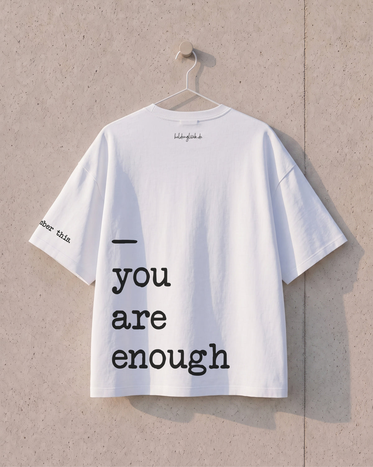 Rückseite des weißen T-Shirts am Bügel, mit großem schwarzem Schriftzug „you are enough“ über mehrere Zeilen.