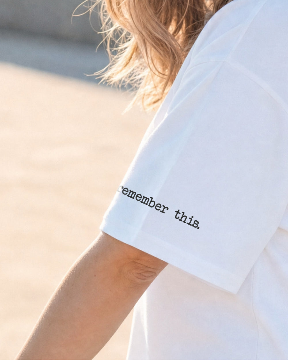 Detail des weißen T-Shirt-Ärmels mit dem schwarzen Schriftzug „remember this.“
