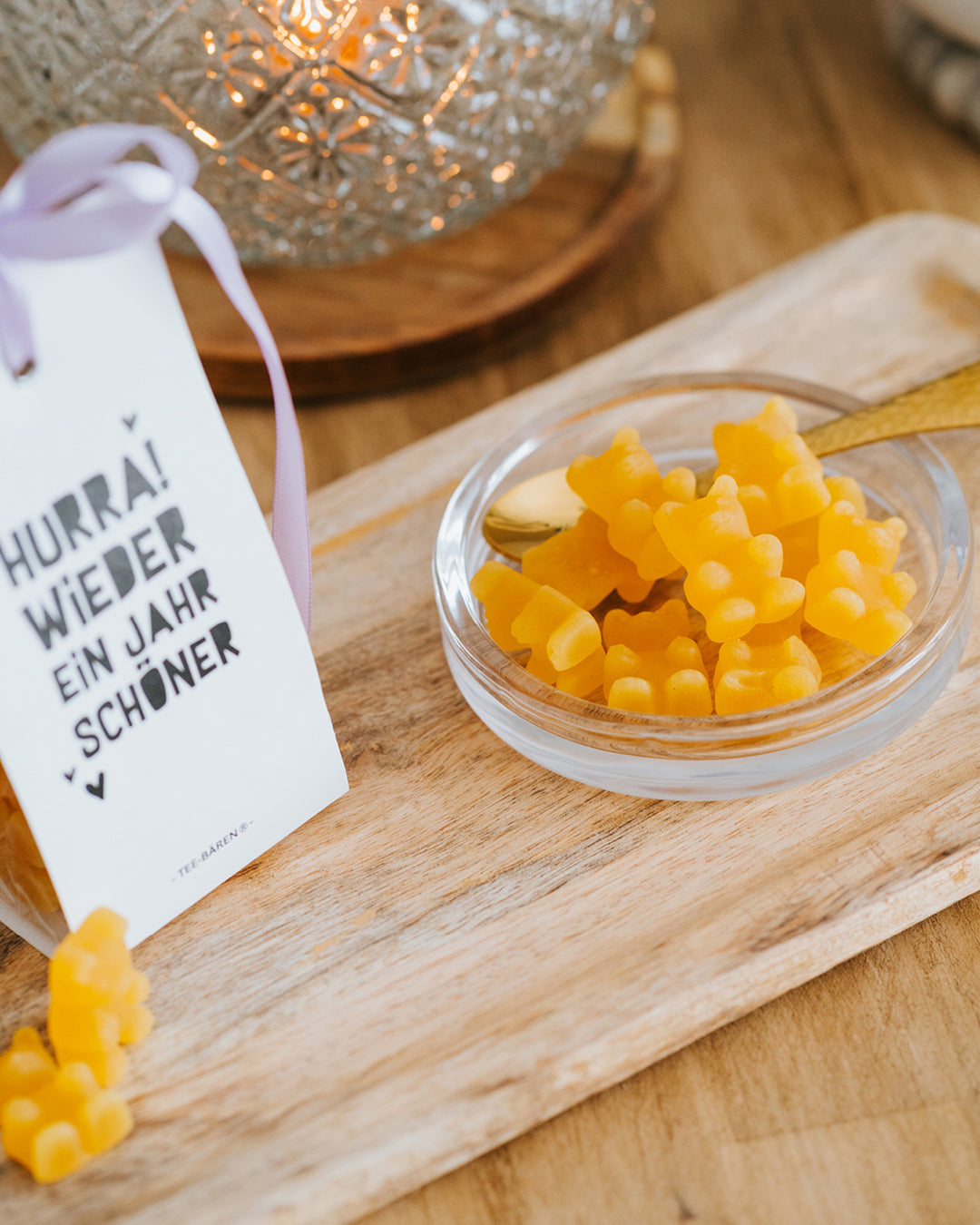 Gelbe Fruchtgummi-Bärchen in der Glasschale mit Goldlöffel, Teebären-Tüte links angeschnitten.