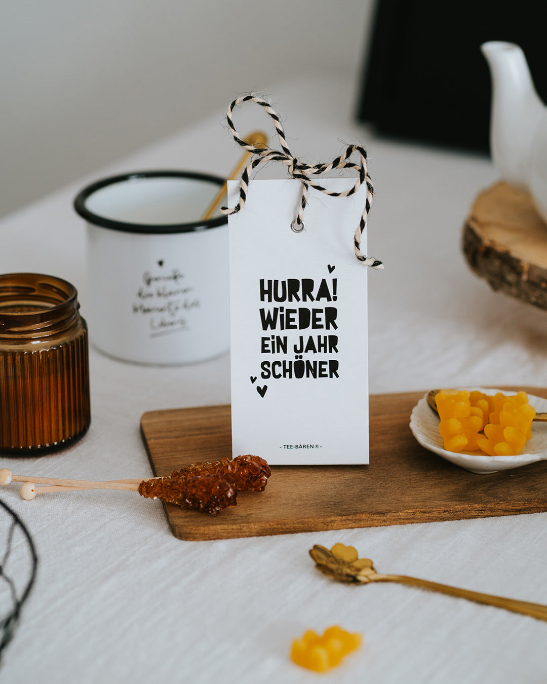 Teebären Hurra! Wieder ein Jahr schöner mit Kordel, daneben Teekanne, Becher und Kandiszucker.