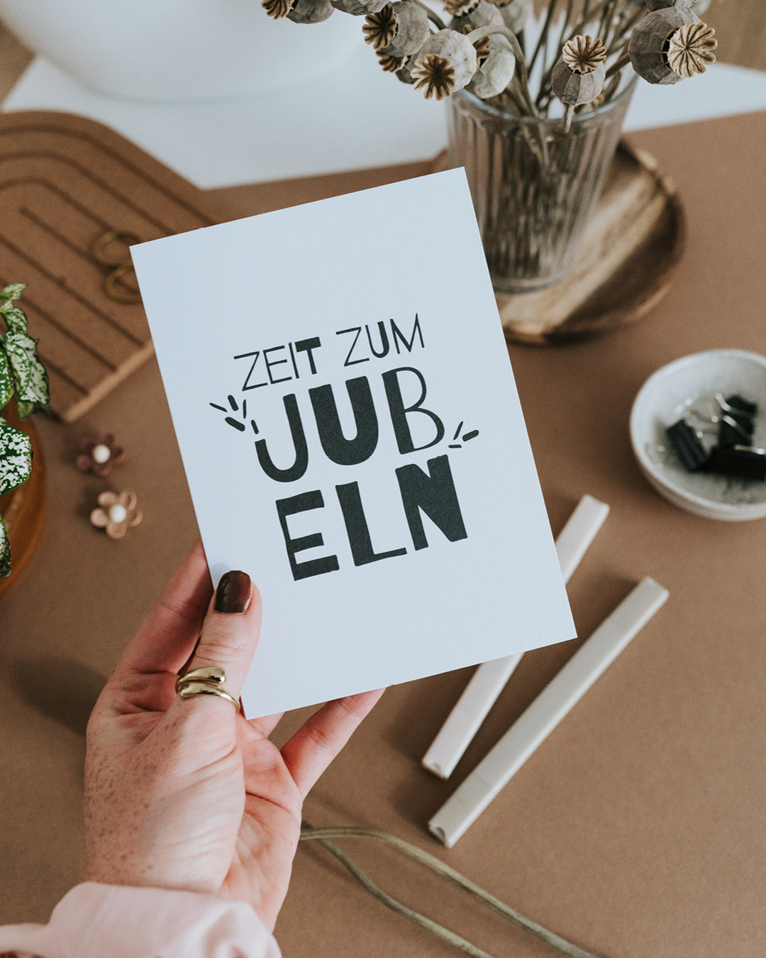 Hand hält Glückwunschkarte „Zeit zum Jubeln" mit markanter Typografie