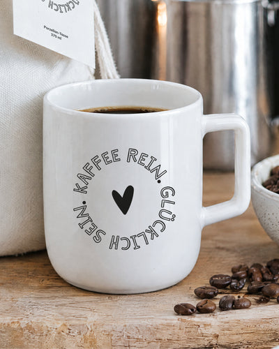 Porzellantasse mit Kaffee und Spruch „Kaffee rein. Glücklich sein.“ mit Herz.