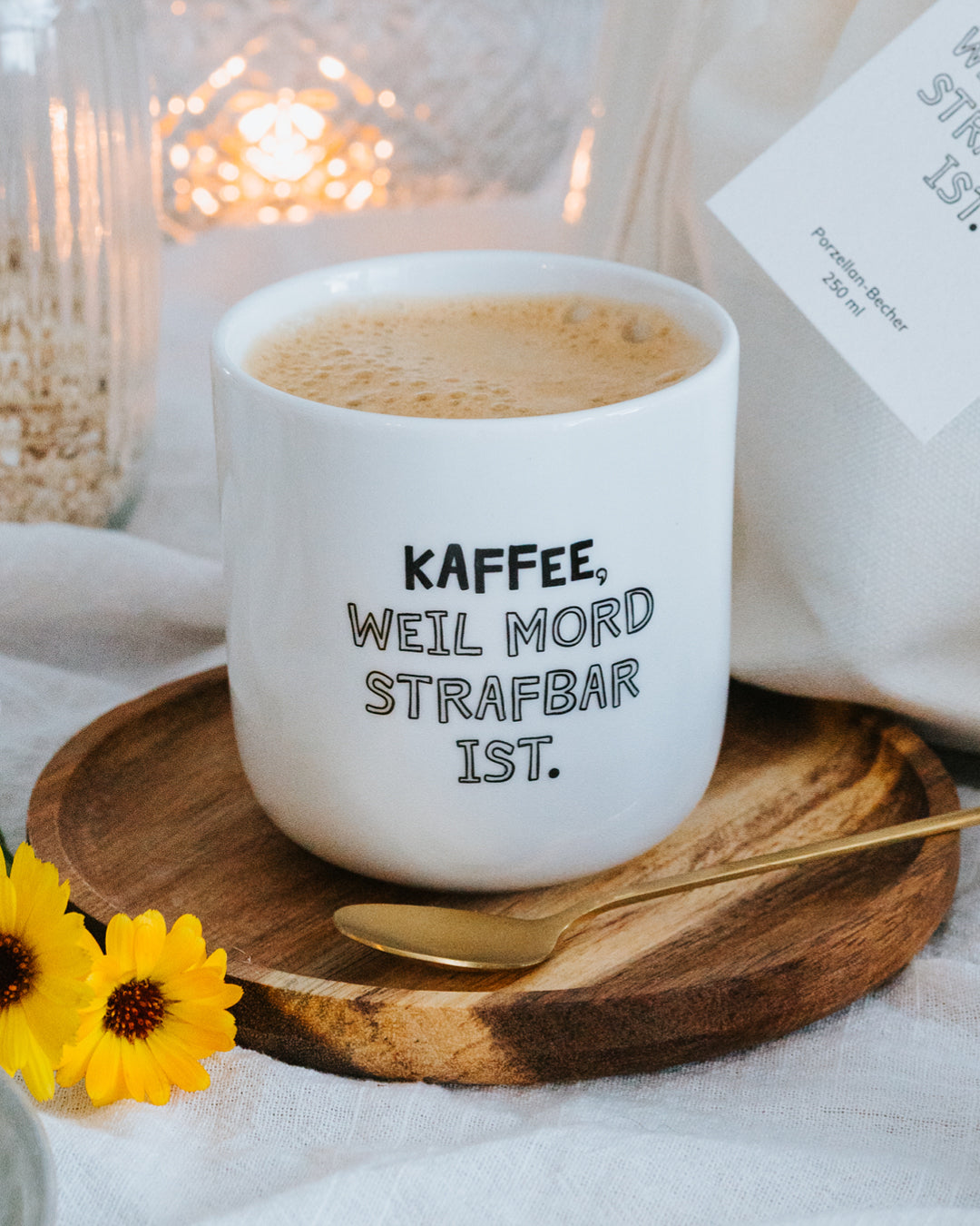 Porzellanbecher „Kaffee, weil Mord strafbar ist.“ mit Milchkaffee auf Holzteller mit Goldlöffel.