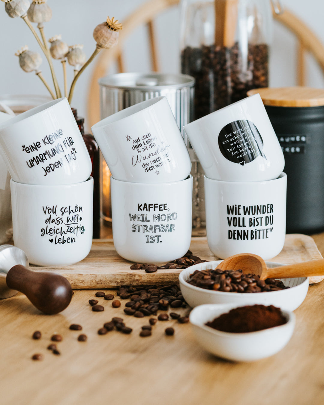 Sechs Heldenglück-Porzellanbecher gestapelt auf Holzbrett mit Kaffeebohnen und Kaffeepulver.