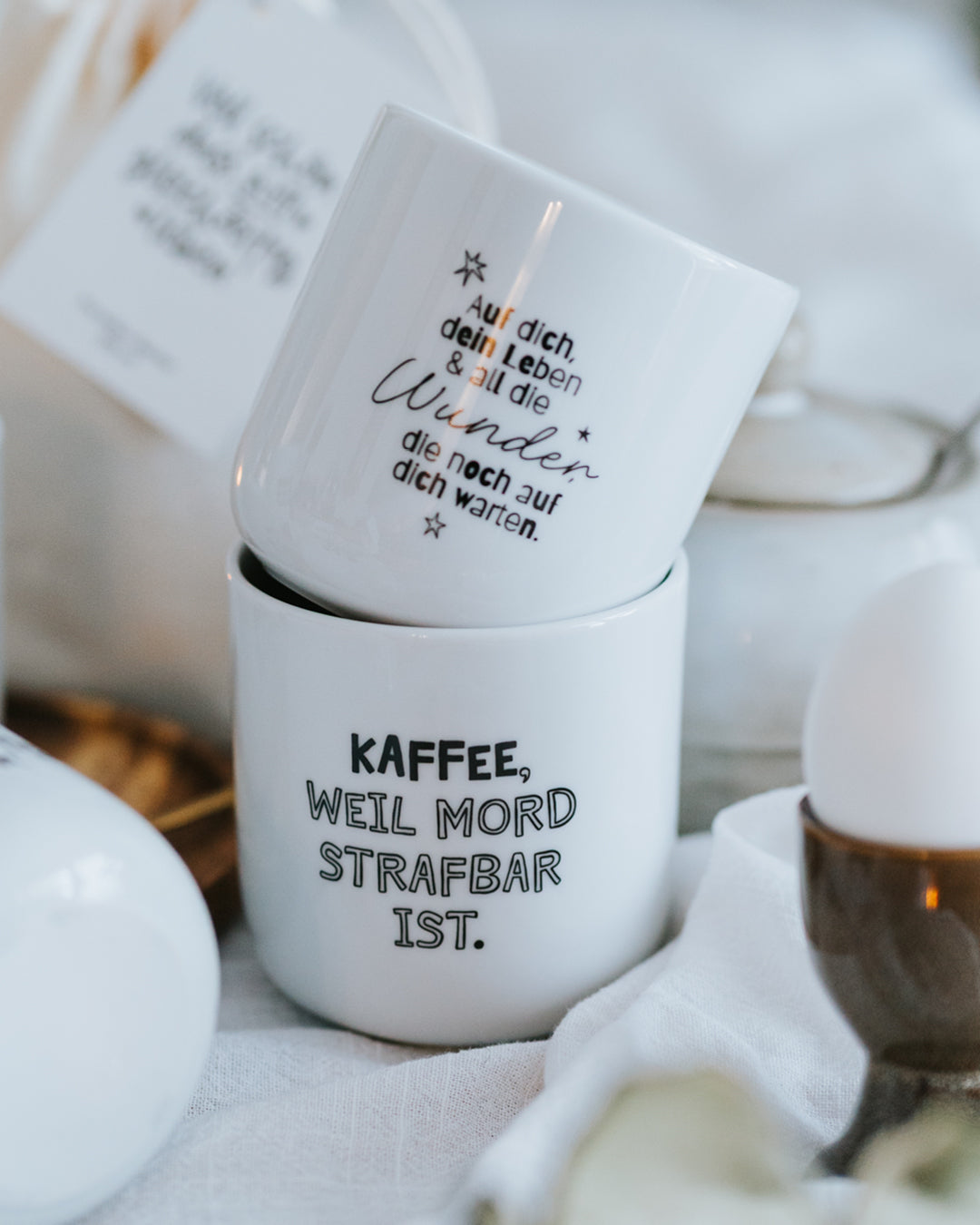Zwei gestapelte Porzellanbecher, „Kaffee, weil Mord strafbar ist.“ vorne – hochwertiges Porzellan, angenehm griffig.