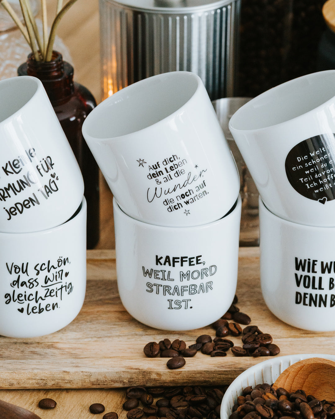 Vier Porzellanbecher gestapelt auf Holzbrett, „Kaffee, weil Mord strafbar ist.“ mittig.