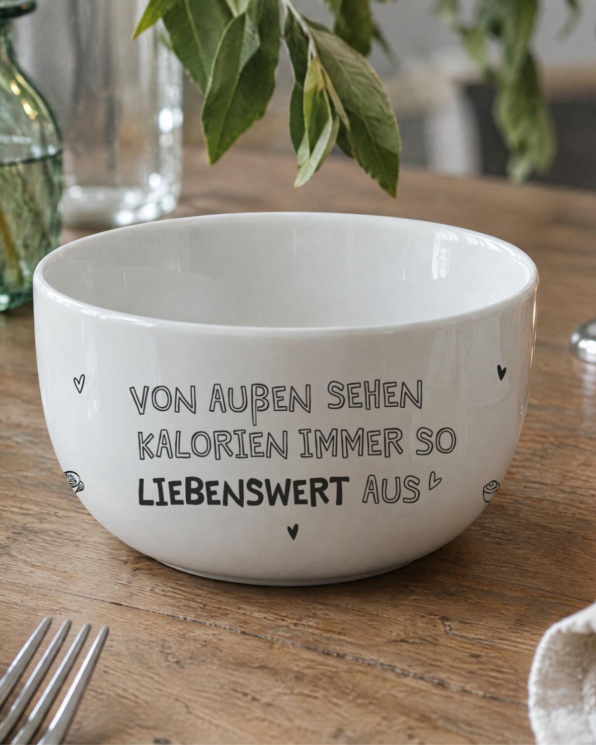 Porzellanschale mit Spruch „Von außen sehen Kalorien immer so liebenswert aus“ auf dem Holztisch.
