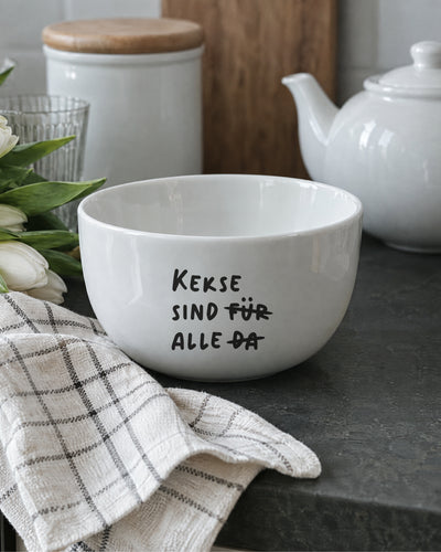 Porzellanschale „Kekse sind für alle da“ neben Teekanne und Tulpen auf der Arbeitsplatte.