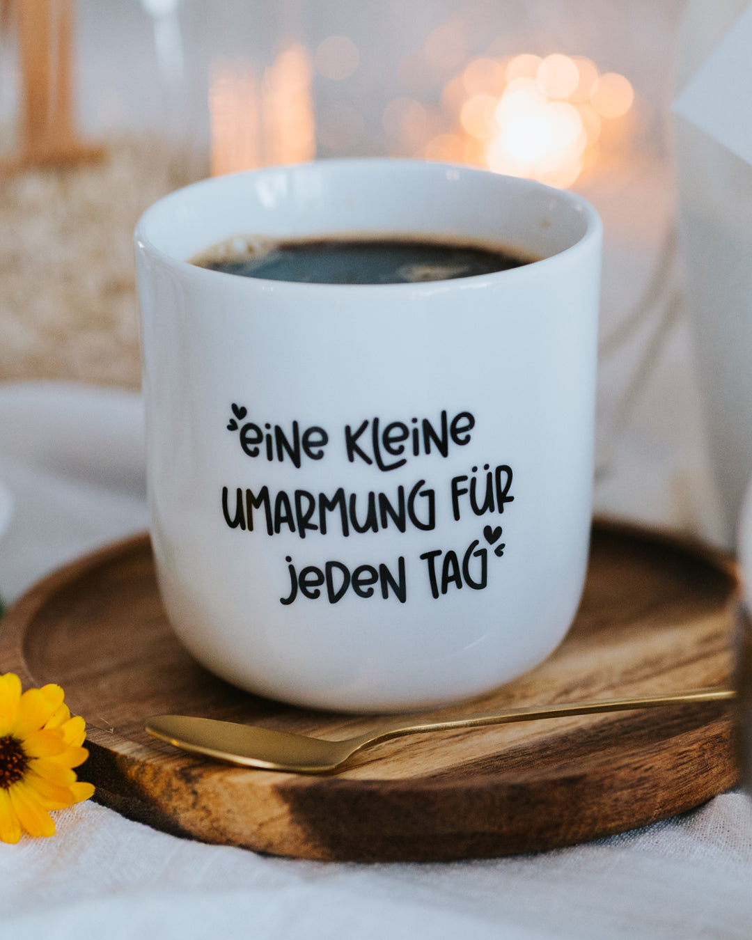 Porzellanbecher „Eine kleine Umarmung für jeden Tag“ mit Kaffee auf Holzteller mit Goldlöffel.