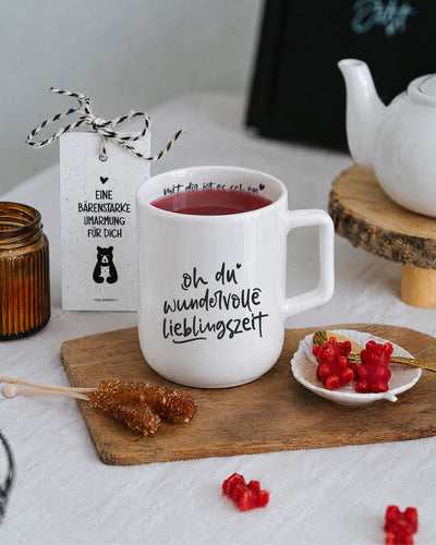 Porzellantasse mit Tee auf Holzbrett, daneben Teebären und Kandiszucker.