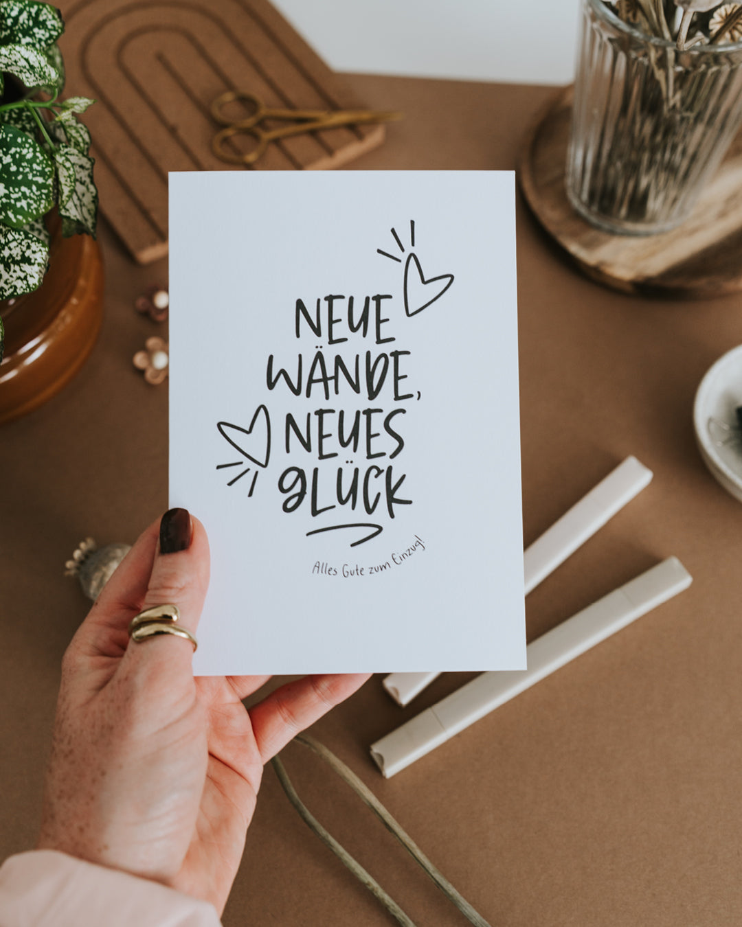 Hand hält Einzugskarte „Neue Wände, neues Glück – Alles Gute zum Einzug" auf hochwertigem Papier