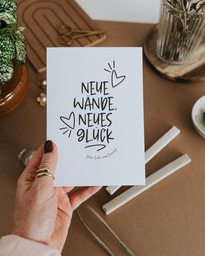 Hand hält Einzugskarte „Neue Wände, neues Glück – Alles Gute zum Einzug" auf hochwertigem Papier