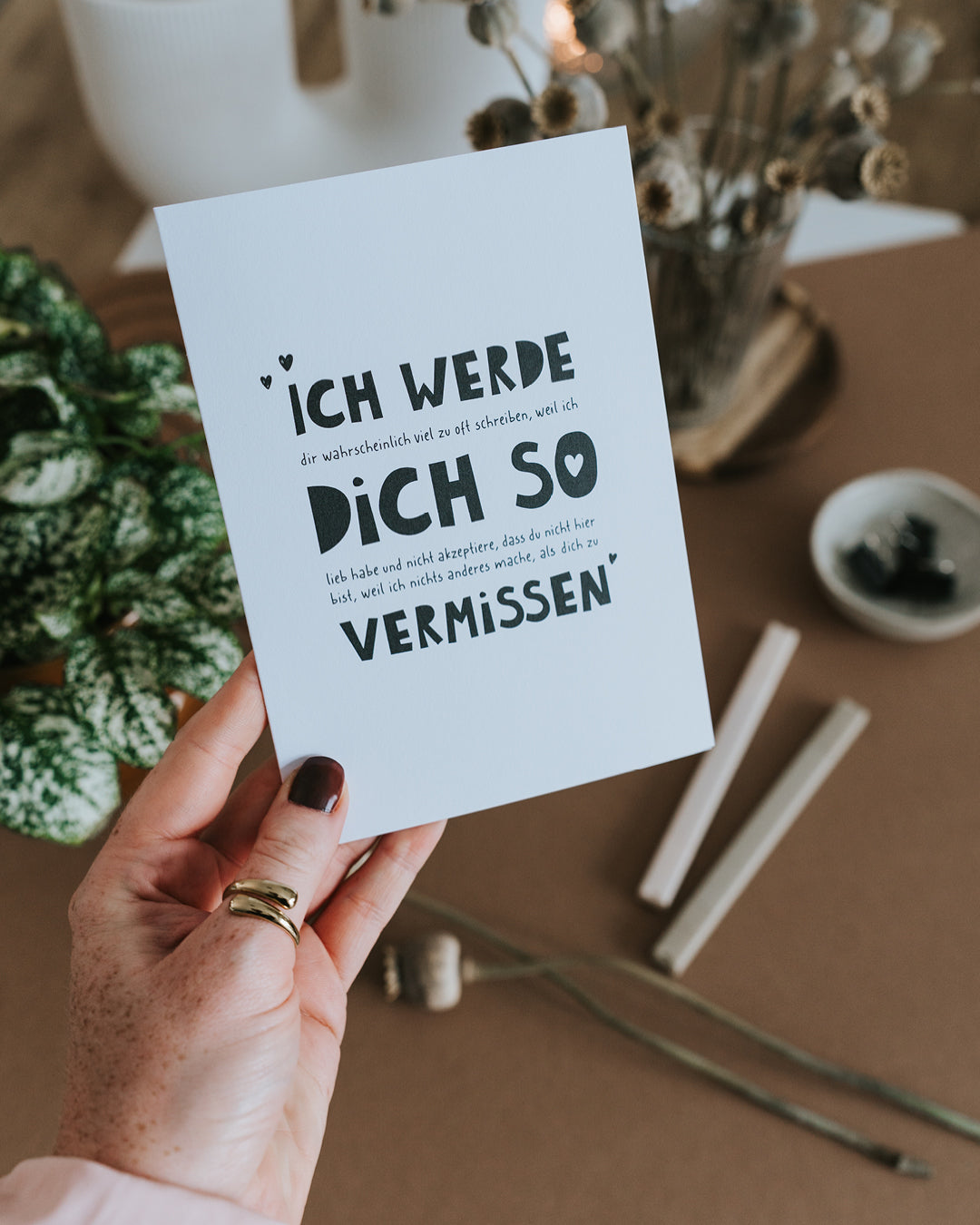 Hand hält Klappkarte „Ich werde dich so vermissen" mit warmem Tex