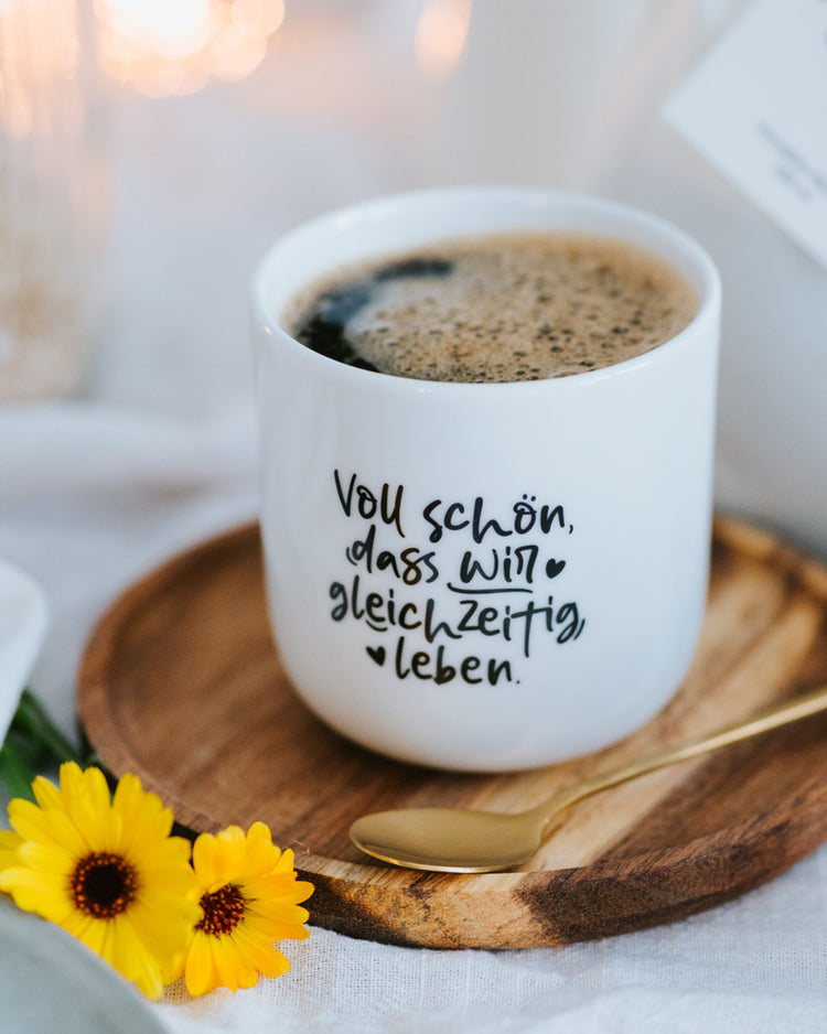 Porzellanbecher „Voll schön“ gefüllt mit Kaffee auf Holzteller – ideal für Kaffee, Tee oder das Büro.