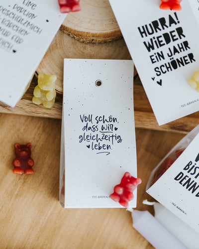 Teebären Voll schön liegend auf Holzscheibe, bunte Fruchtgummi-Bärchen verstreut.