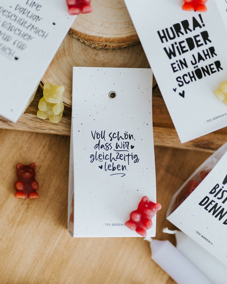 Teebären Voll schön liegend auf Holzscheibe, bunte Fruchtgummi-Bärchen verstreut.