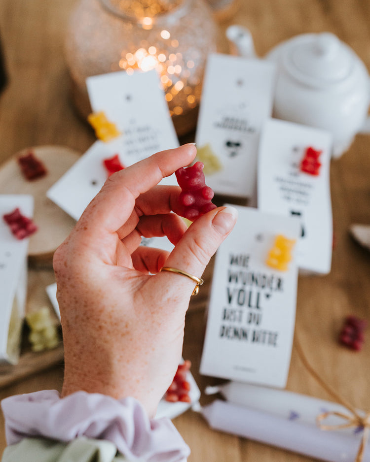 Hand hält ein dunkelrotes Teebärchen als Größenreferenz, Geschmack Cranberry-Vanille.