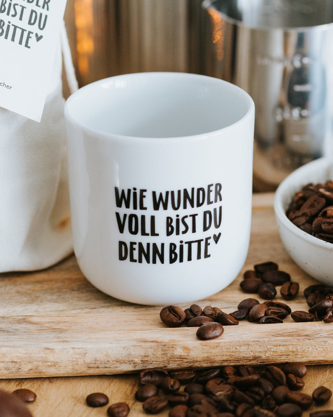 Porzellanbecher „Wie wundervoll bist du denn bitte“ auf Holzbrett mit Kaffeebohnen – zeitloses Design.